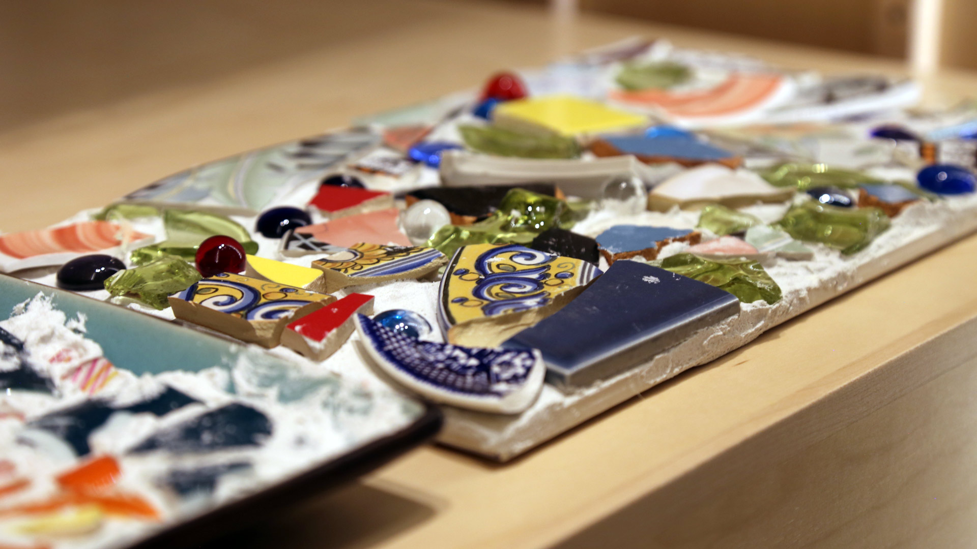 a close-up of one of the mosaics in the left case featuring broken plates, glass beads, and other materials