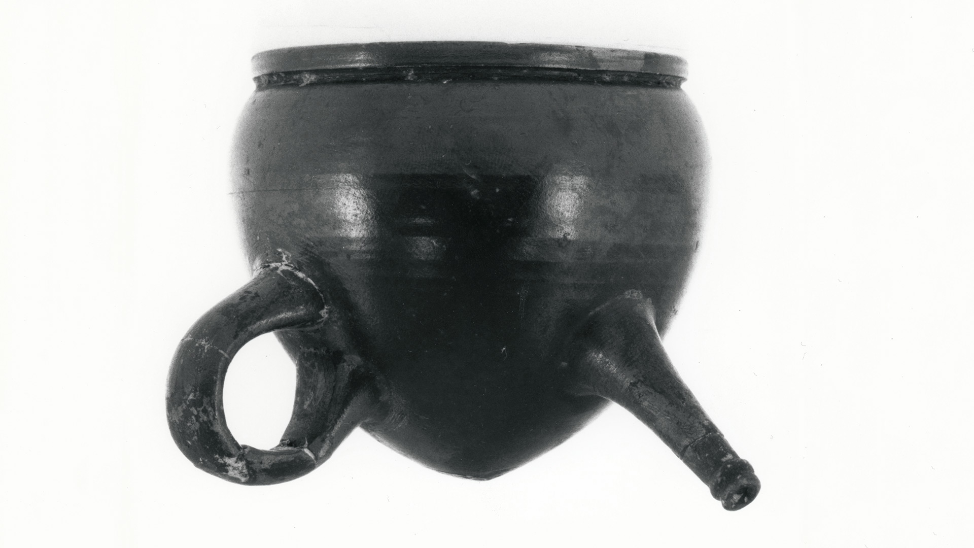 A heavy black metal closed pot with finger loop and spout