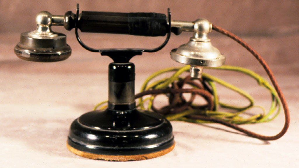 An old-style phone with brass ended handset resting on black base and straight red and gold cord